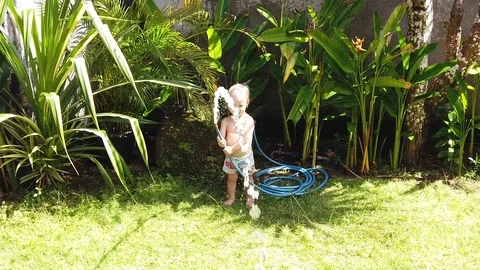  two-year-old child holding a garden watering hose in his hands  Stock Footage 107906688