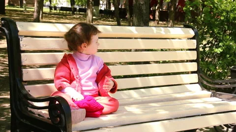 Two year old child is sitting on the bench corrects hair and looks to the right Stock Footage 90265035