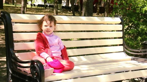 Two year old child is sitting on the bench corrects hair and smile. She Stock Footage 90265149