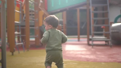A two-year-old child walks on a playground among slides and swings. Little son Stock Footage 242446325
