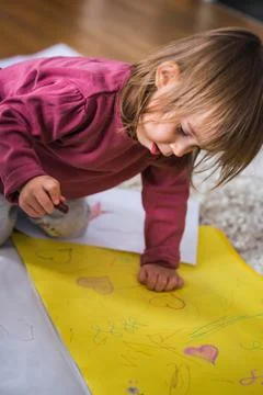 Two year old drawing on papper with wax crayons, sitting on floor indoors. Stock Photos