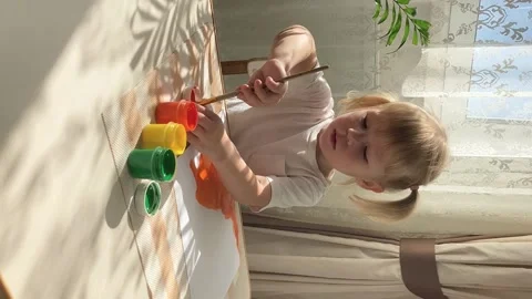 A two-year-old girl in , drawing with orange gouache paints. Stock Footage 208040428