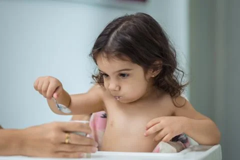 Two year old girl eats yogurt with a spoon, middle plane Stock Photos
