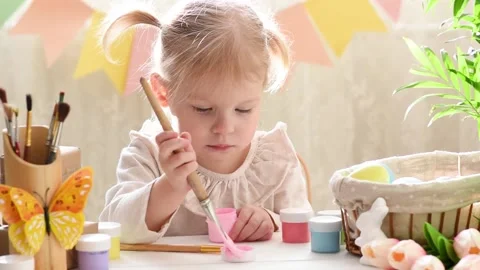 A two-year-old girl with two tails paints an Easter egg with pink paint Stock Footage 175516815