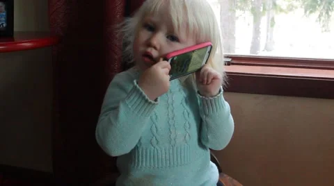 Two year old sits listening to backside of a smart phone Stock Footage 44021474