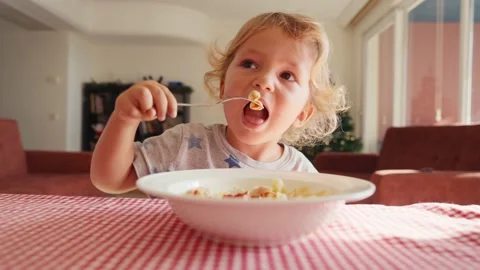 Two year old smiling baby boy sits at table in highchair and eats pasta with Stock-Footage 228719735