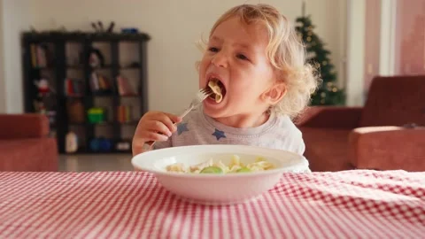 Two year old smiling baby boy sits at table in highchair and eats pasta with 動画素材 228719762