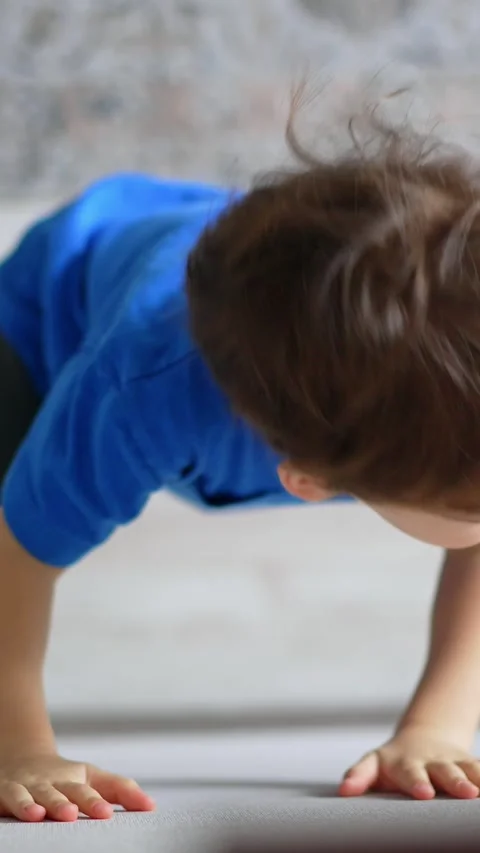 Two-year old toddler standing at the wall trying to climb it. Kid fail and sits Stock Footage 332346382