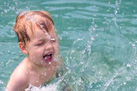 Two years old boy is splashing the water in the swimming pool Stock Photos