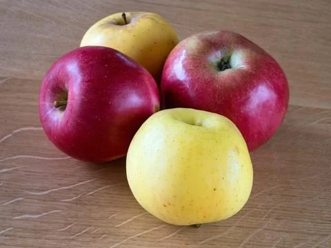 Two yellow and two red apples on a wooden table. Foto stock