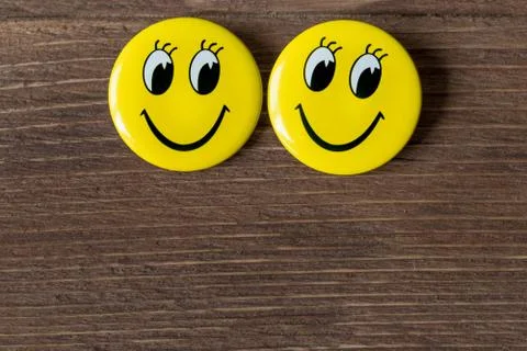 Two yellow buttons with smiley faces on a wooden background. Close up Stock Photos
