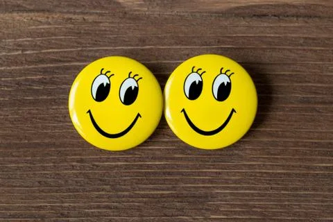 Two yellow buttons with smiley faces on a wooden background. Top view Stock Photos