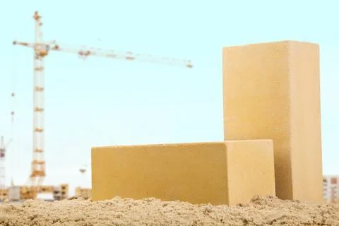 Two yellow ceramic bricks on the sand at the building background with crane Stock Photos