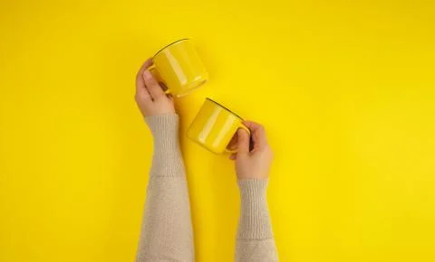 Two yellow ceramic cups are supported by a female hand on a yellow background Stock Photos