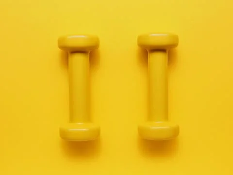 Two yellow dumbbells on a yellow background Stock Photos