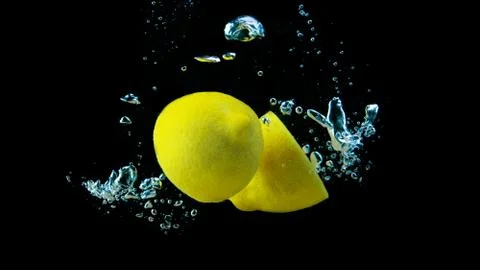 Two yellow lemon halves falling into water with air bubbles on black backgrou Stock Photos