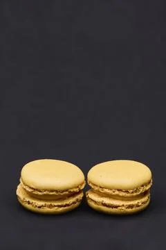Two yellow macarons isolated on dark background minimalist food photo Foto stock