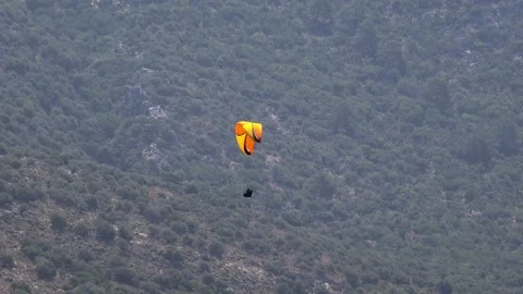 Two yellow orange Spanish paragliders glide down beside a scrub forest mountain Stock Footage 339367698
