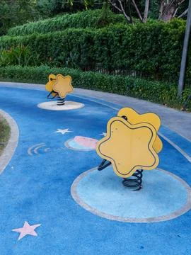 Two yellow star shaped spring riders on a blue playground pathway symbolizi.. Stock Photos