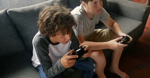 Two young 11 - 13 year old boys sitting on a sofa playing video games Видео 85373787