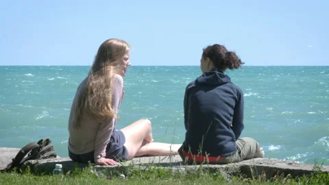 Two Young Adult Female Friends Talking Sitting at the Beach Stock Footage