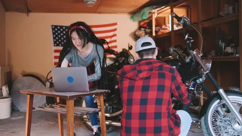 Two young adults are focused on a motorcycle project in a garage, with one using Stock Footage 313848591