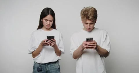 Two young adults stand next to each other, both engaged with their smartpho.. Stock Footage 313273699