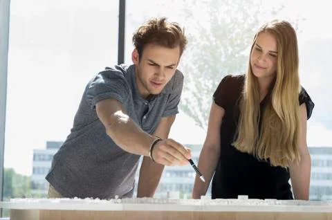 Two young architects standing at a table, working on an architectural model. Stock Photos