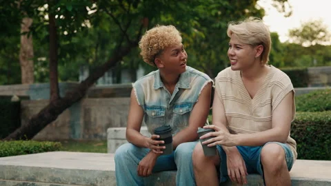 Two young Asian friends chatting and holding coffee cups while sitting on a Stock Footage 278721247