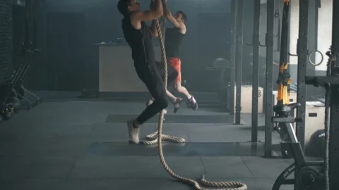 Two young athletic people dowing pull-ups on rope climbing together in spacious Stock Footage 104578951