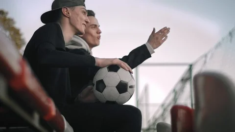 Two young attractive guys sitting on the chairs of an empty stadium, talking Stock Footage 114132015