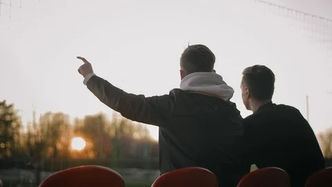 Two young attractive guys sitting on the chairs of an empty stadium, talking Stock Footage 114132090