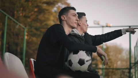 Two young attractive guys sitting on the chairs of an empty stadium, talking Stock Footage 114132091