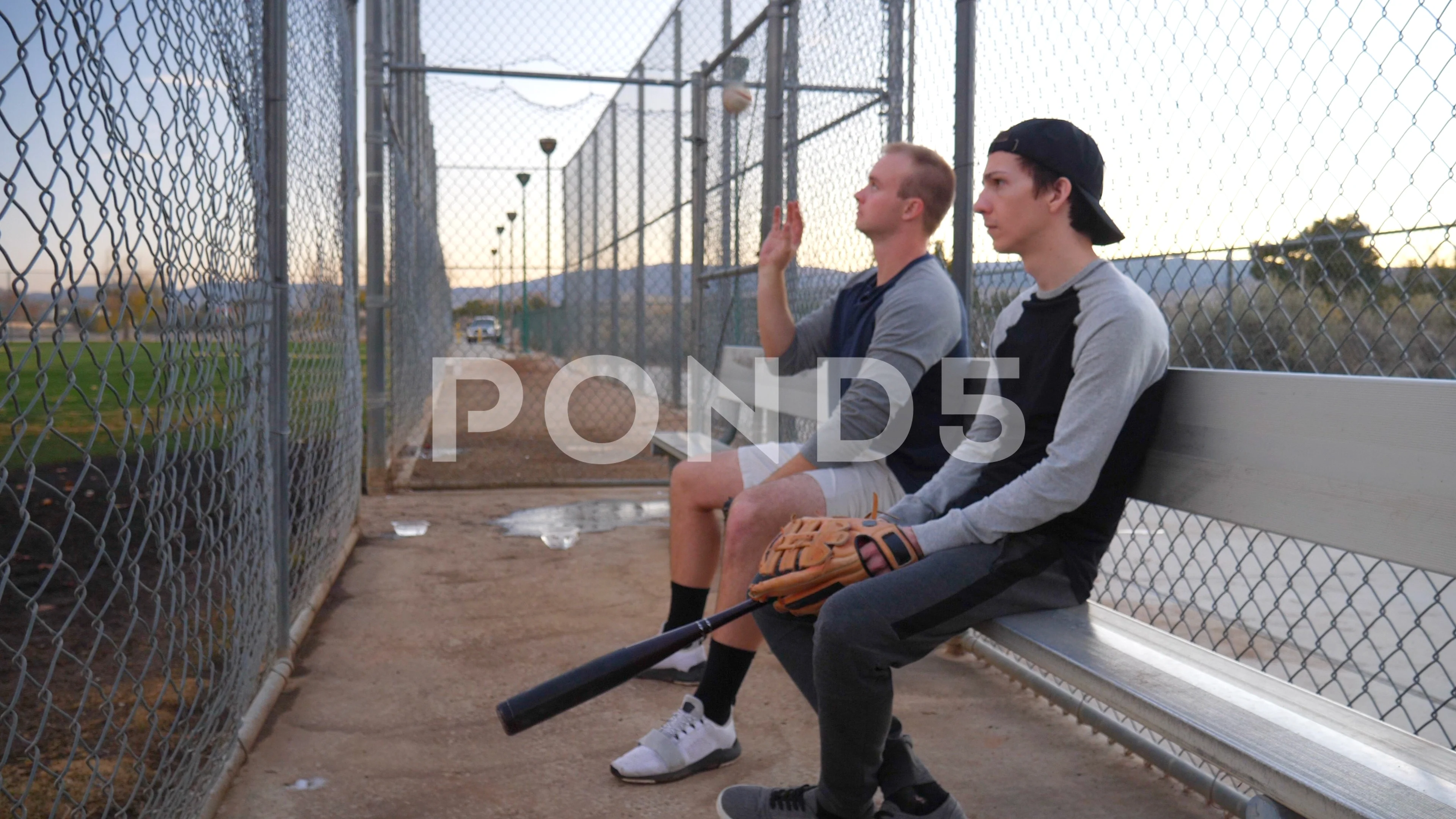 A young, black baseball player sits in the dugout during a