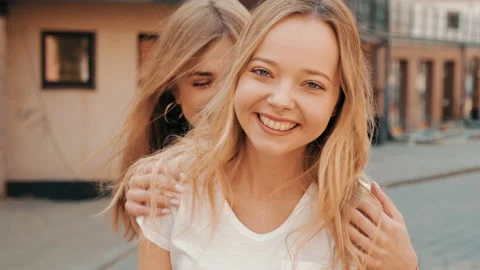 Two young beautiful blond smiling hipster girls in trendy summer clothes Stock Footage 141220209