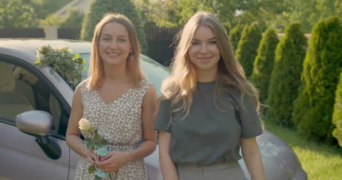 Two young beautiful girls, wearing casual clothes, in front of car, smiling Stock Footage 134630853