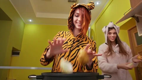 Two young beautiful happy smiling girls jump around pan, bring fresh vegetables Stock Footage 77261064