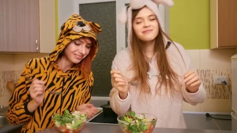 Two young beautiful happy smiling girls jump, dance and eat salads with fresh Vídeo Stock 77261531