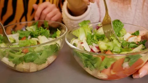 Two young beautiful happy smiling girls jump, dance and eat salads with fresh Stock Footage 77262202