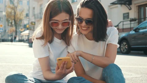 Two young beautiful smiling hipster female with smartphone outdoors Stock Footage 154904006