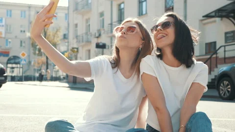 Two young beautiful smiling hipster female taking selfie outdoors Stock Footage 154904547
