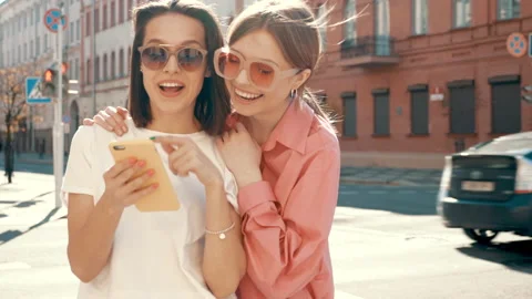 Two young beautiful smiling hipster female using phone outdoors Stock Footage 154906629