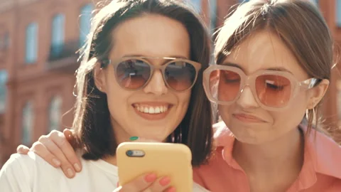 Two young beautiful smiling hipster female using phone outdoors at sunset Stock Footage 154906701