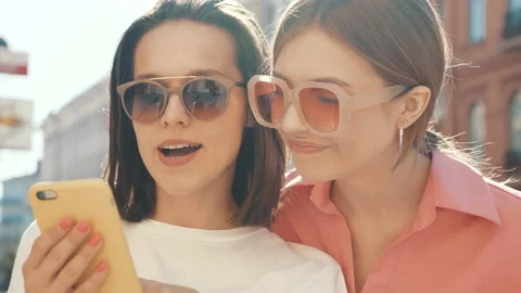 Two young beautiful smiling hipster female using phone at sunset Stock Footage 154906892