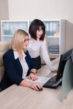 Two young beautiful weman work in the office. Copmuter teamwork. Stock Photos