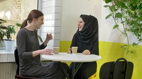 Two young beautiful womans sitting in cafe and laughing, one of them muslim Video stock 90609254