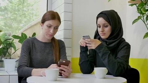 Two young beautiful womans sitting in cafe and typing on phones, one of them Video stock 90614853