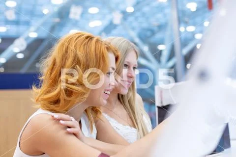Two young beautiful women in a travel agency choosing a vacation trip, using the Stock Photos