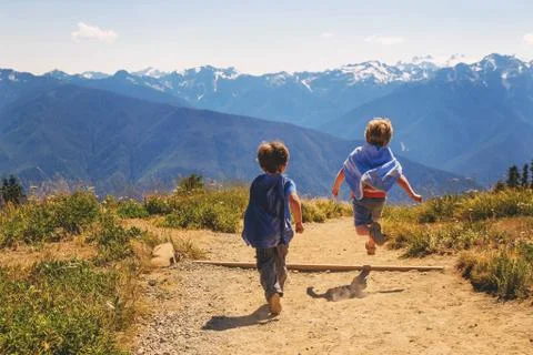 Two young boys (2-3, 4-5) wearing super hero capes running on mountain Stock Photos