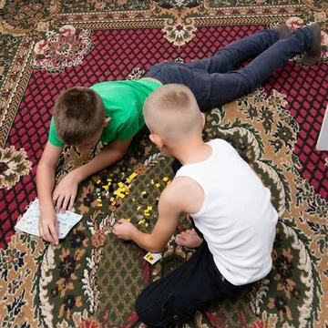 Two young boys are lying on a rug, focused on building with tiny blocks. Thei Stock Photos